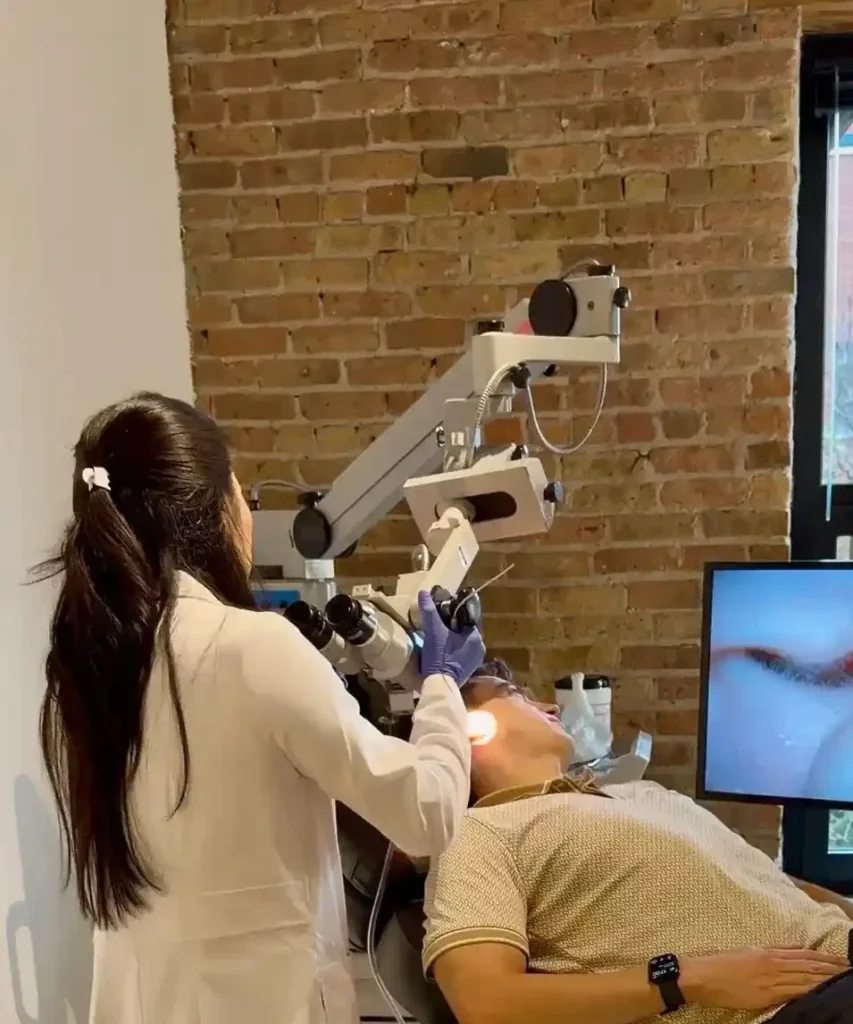 A physician assistant uses a microscope to examine a patient in an examination chair. The patient is a man in his 30s and is having earwax cleaning procedure in Chicago, IL